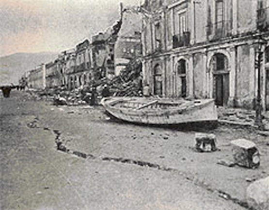 I palazzi sono distrutti, uno squarcio corre lungo la strada, un uomo si riposa su una barca trascinata a terra dal maremoto